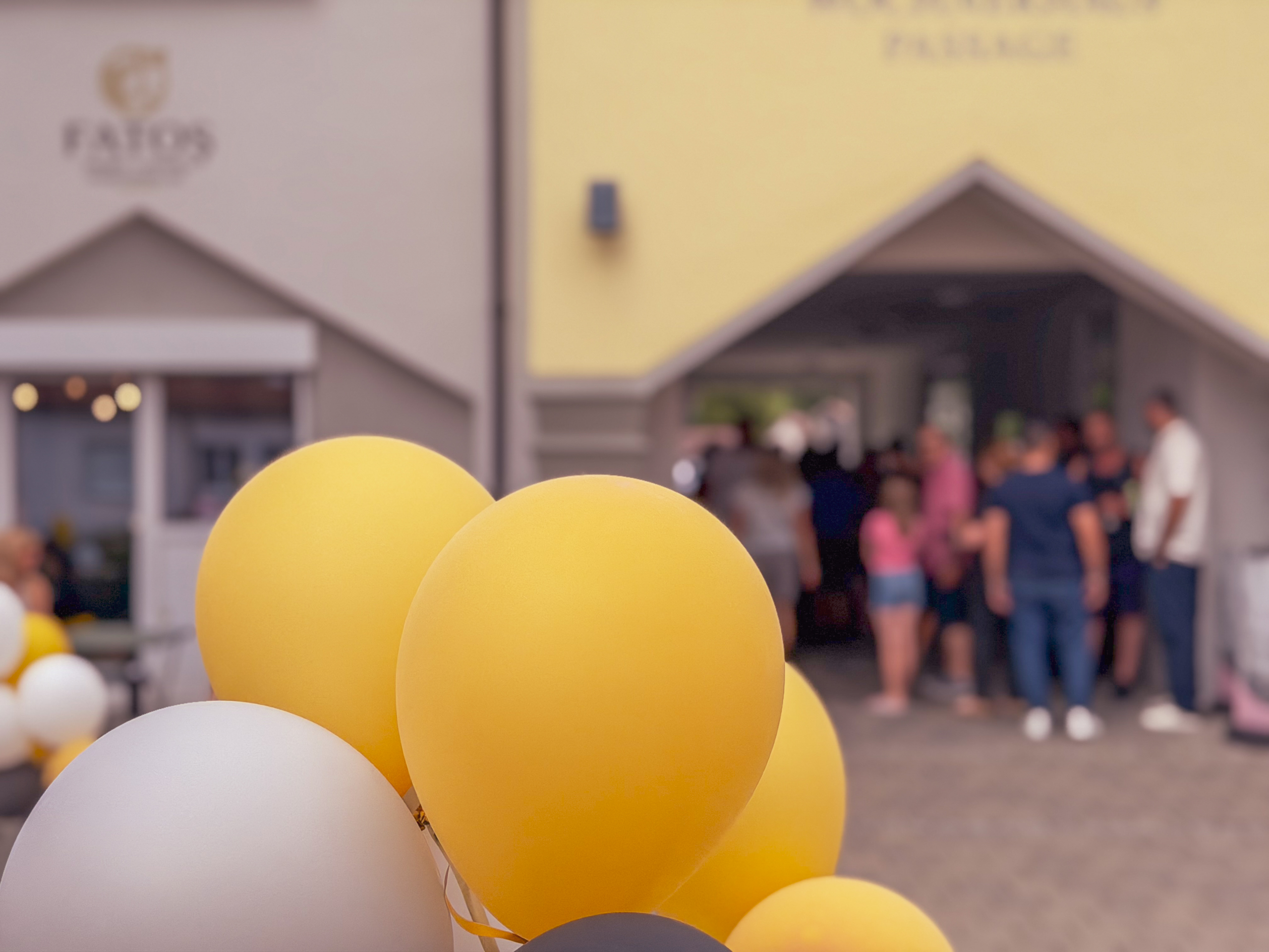 Gelbe und weiße Ballons vor dem Salon-Eingang mit Gästen im Hintergrund